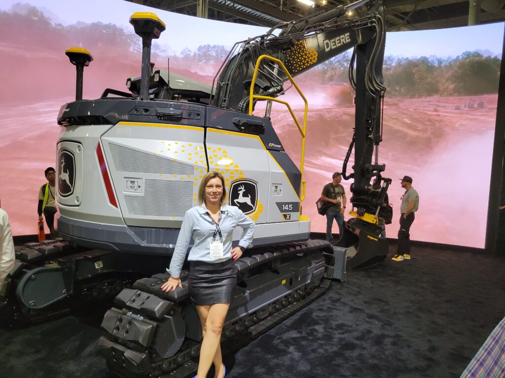 Amanda from Burgex stands next to a new John Deer electric excavator.